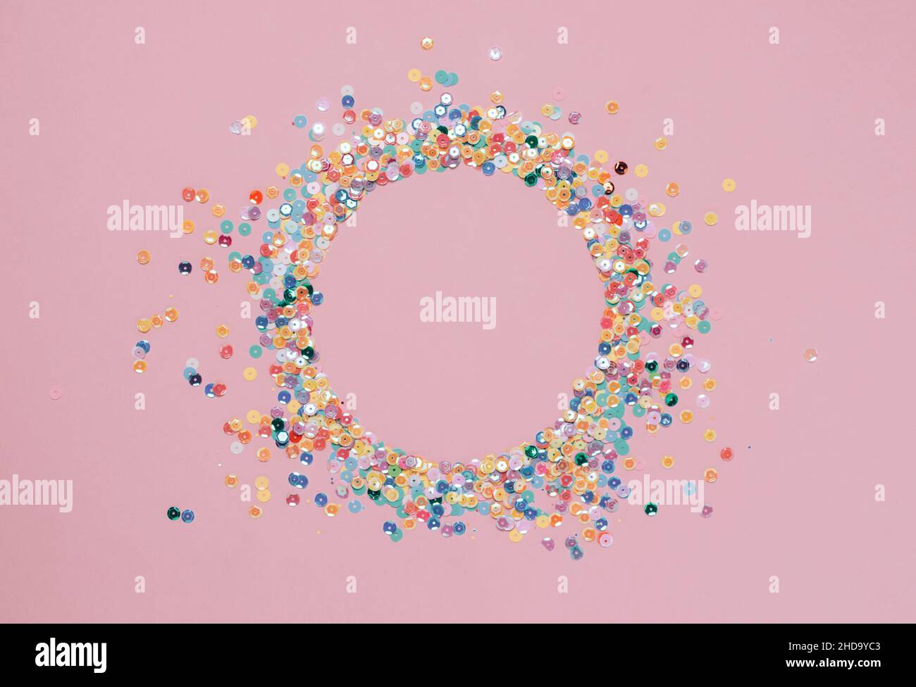 Sequins multicolored confetti lined in round frame pink background. Abstract festive composition place for text Stock Photo