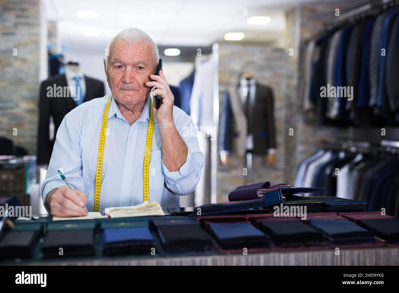 Professional tailor man talking on mobile phone and making notes in notebook Stock Photo