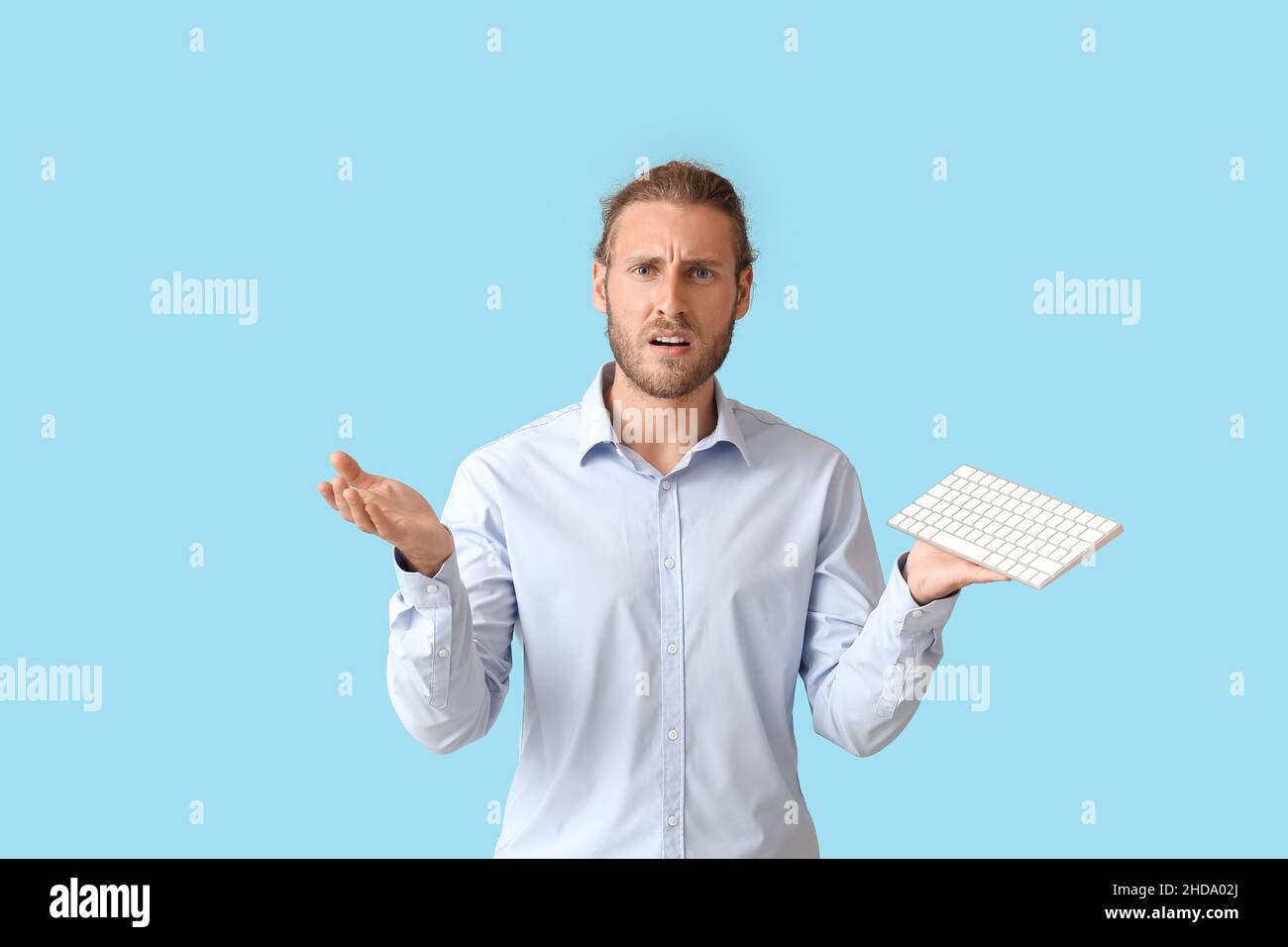 Confused man with keyboard on color background Stock Photo
