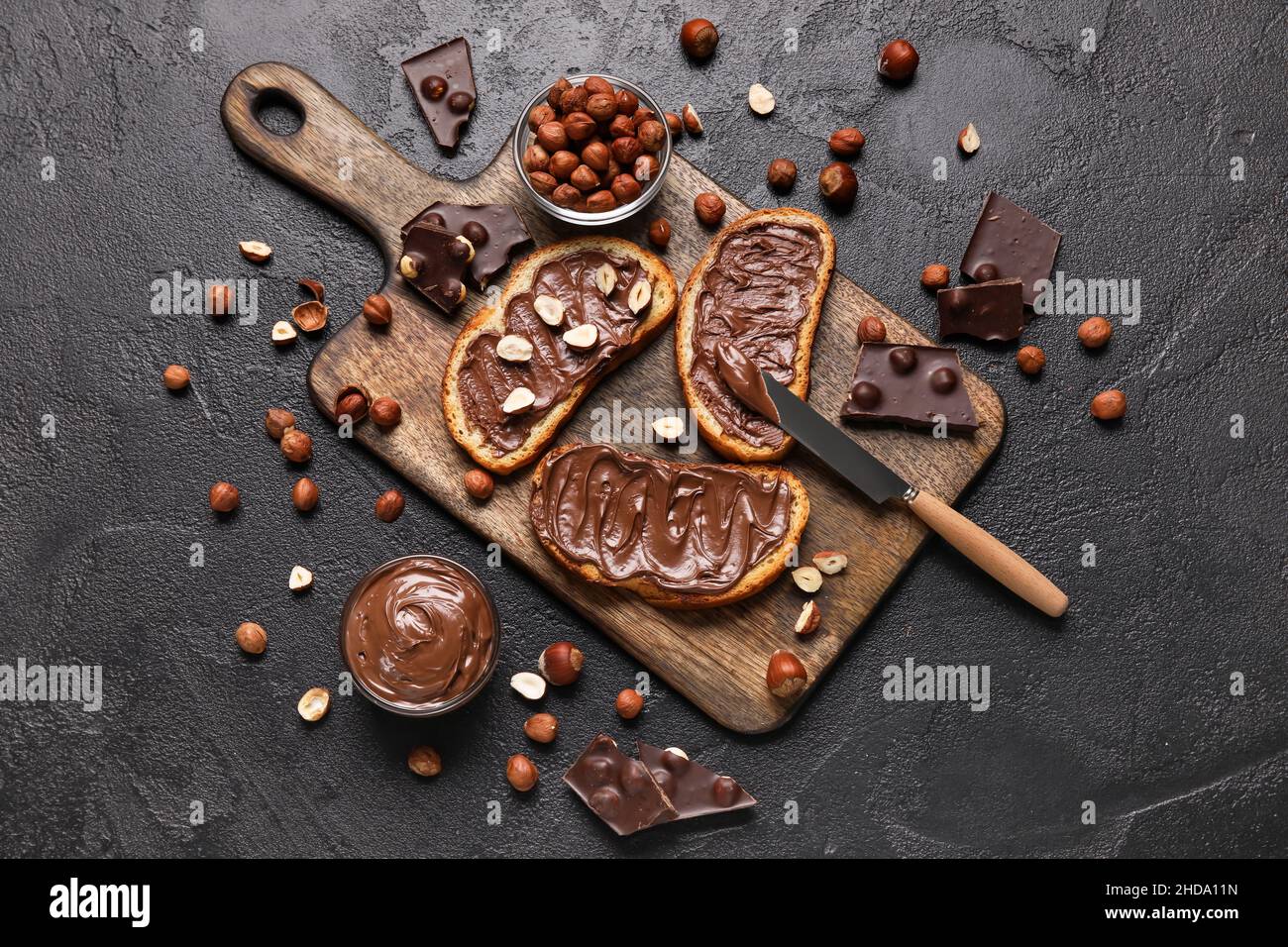 Wooden board of bread with chocolate paste and hazelnuts on black ...