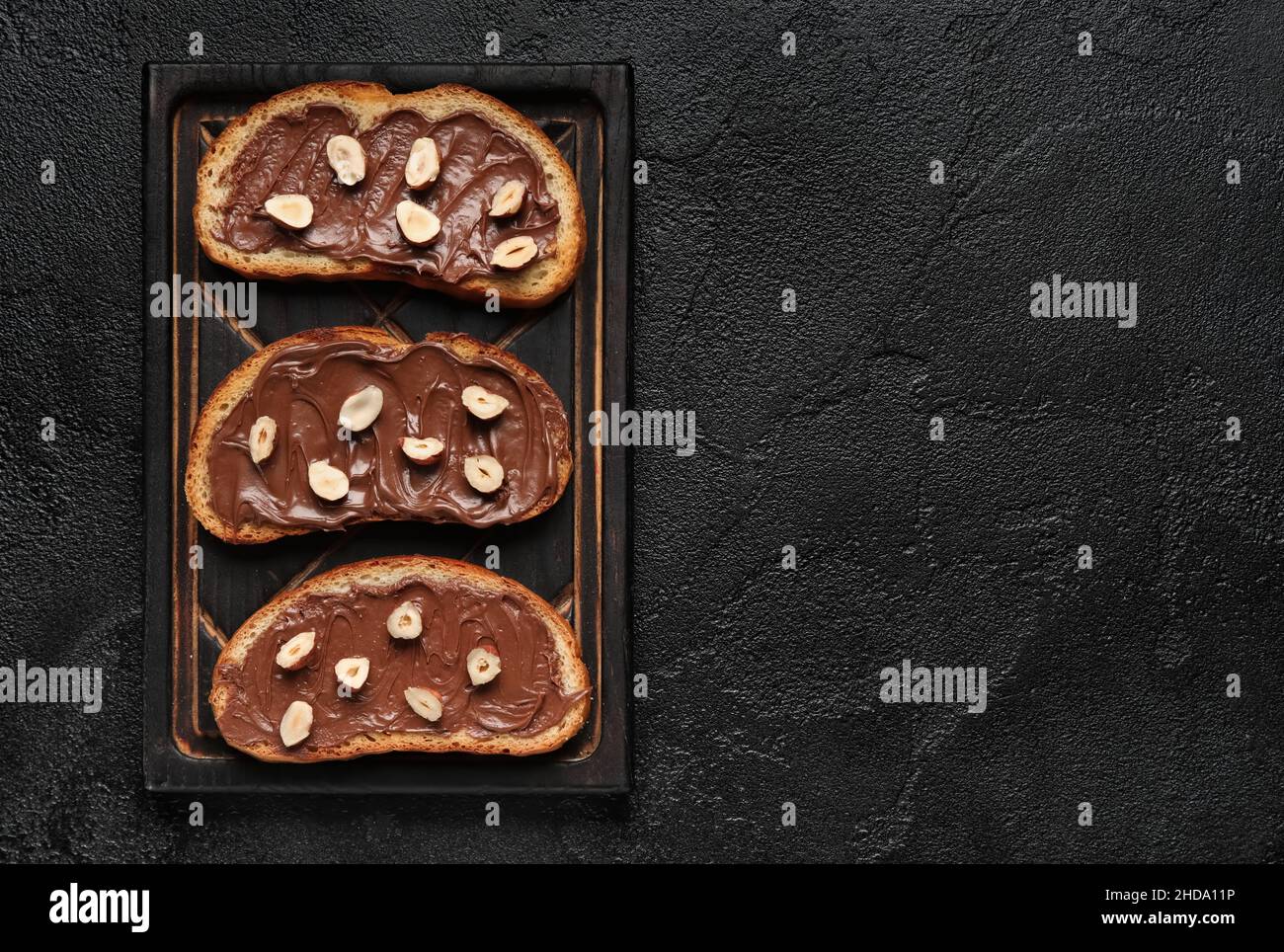 Wooden board of bread with chocolate paste and hazelnuts on black ...