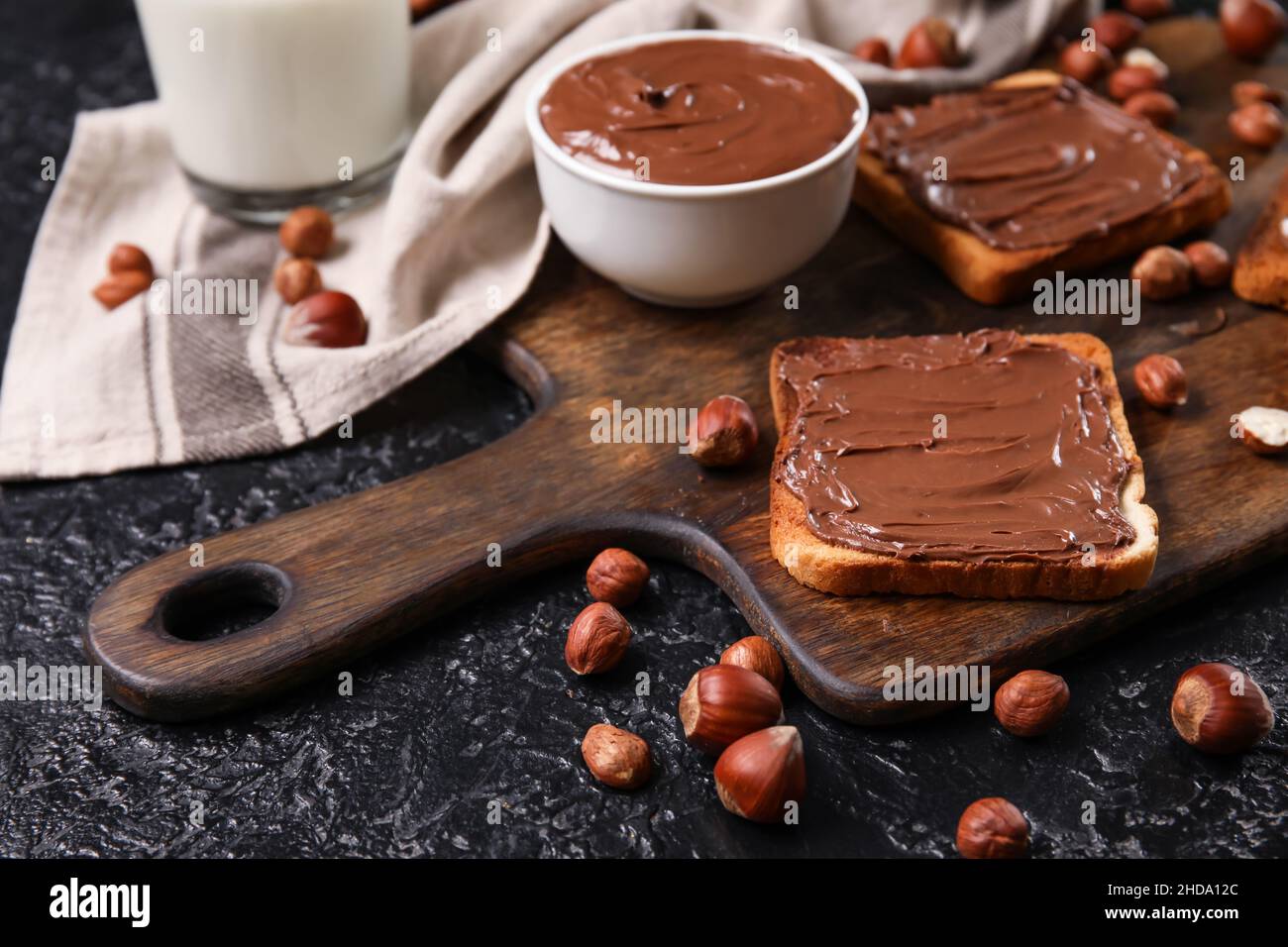 Wooden board of bread with chocolate paste and hazelnuts on black ...