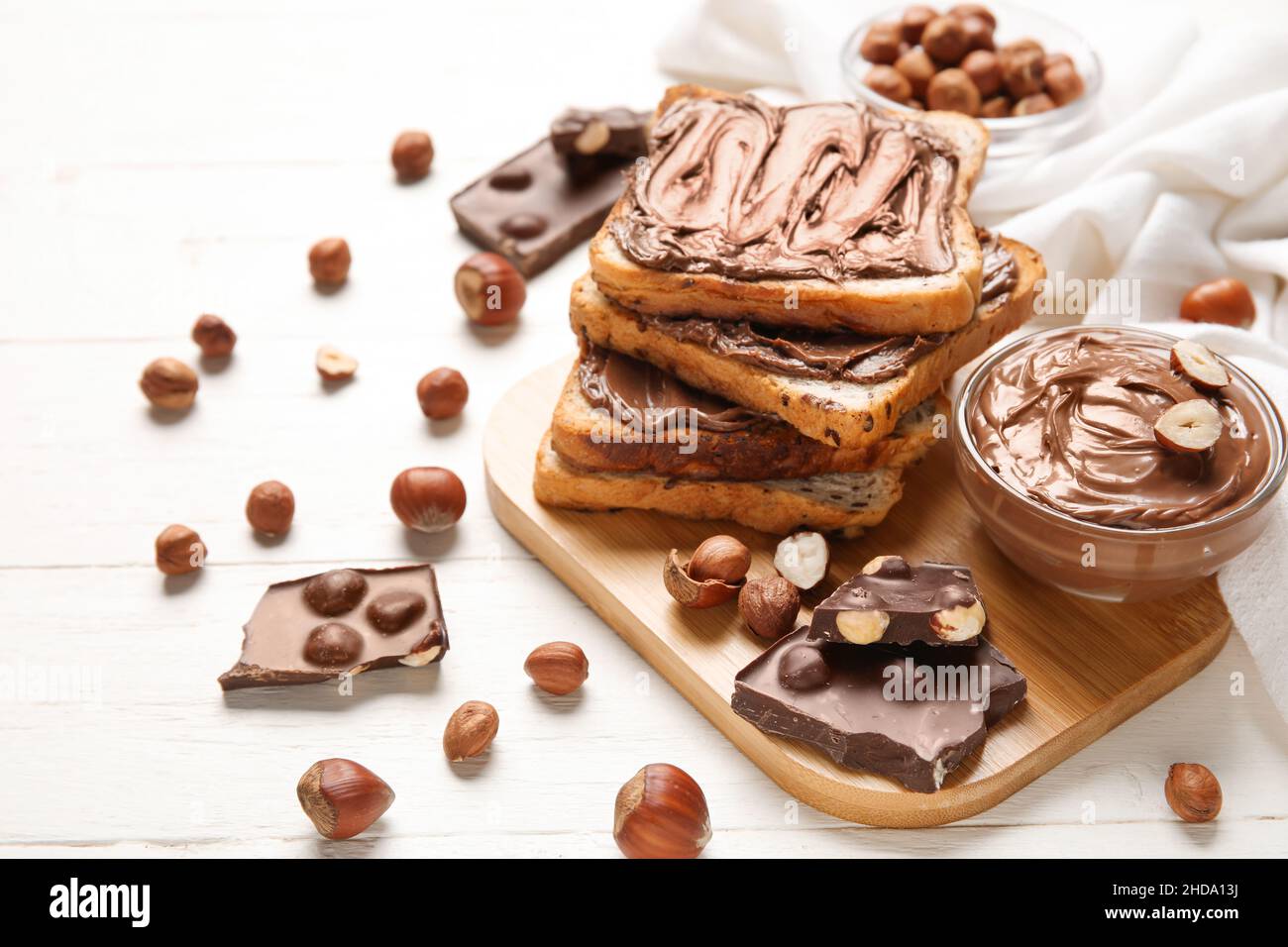 Board of bread with chocolate paste and hazelnuts on white wooden ...