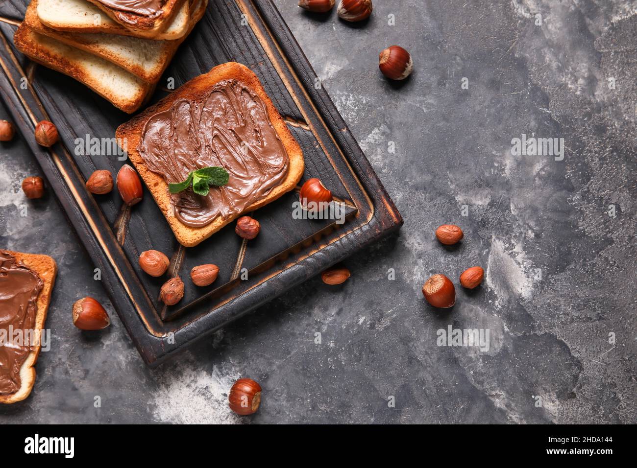 Wooden board of bread with chocolate paste and hazelnuts on black ...