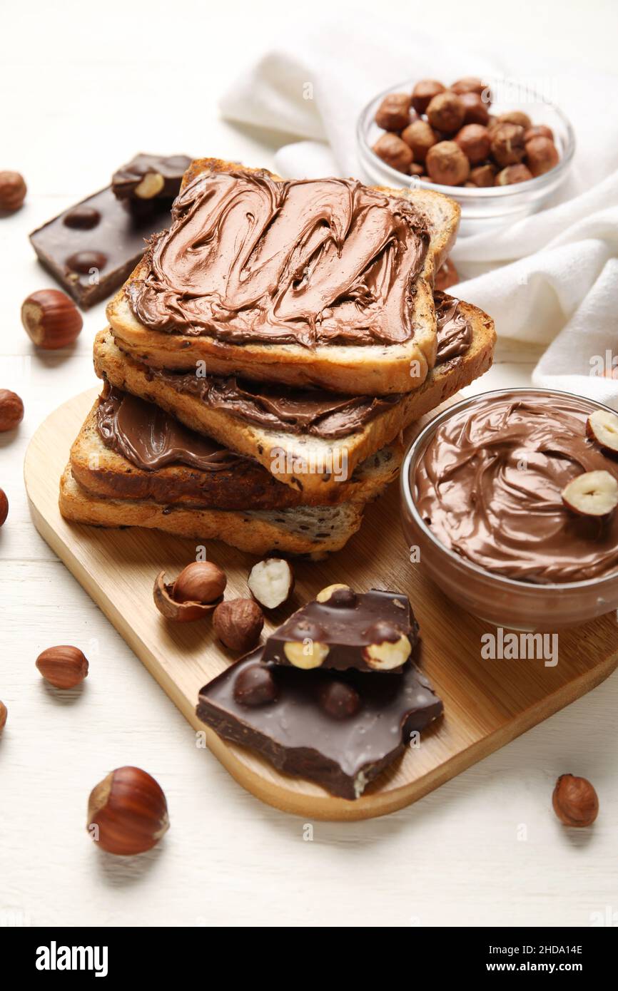 Board of bread with chocolate paste and hazelnuts on white wooden ...