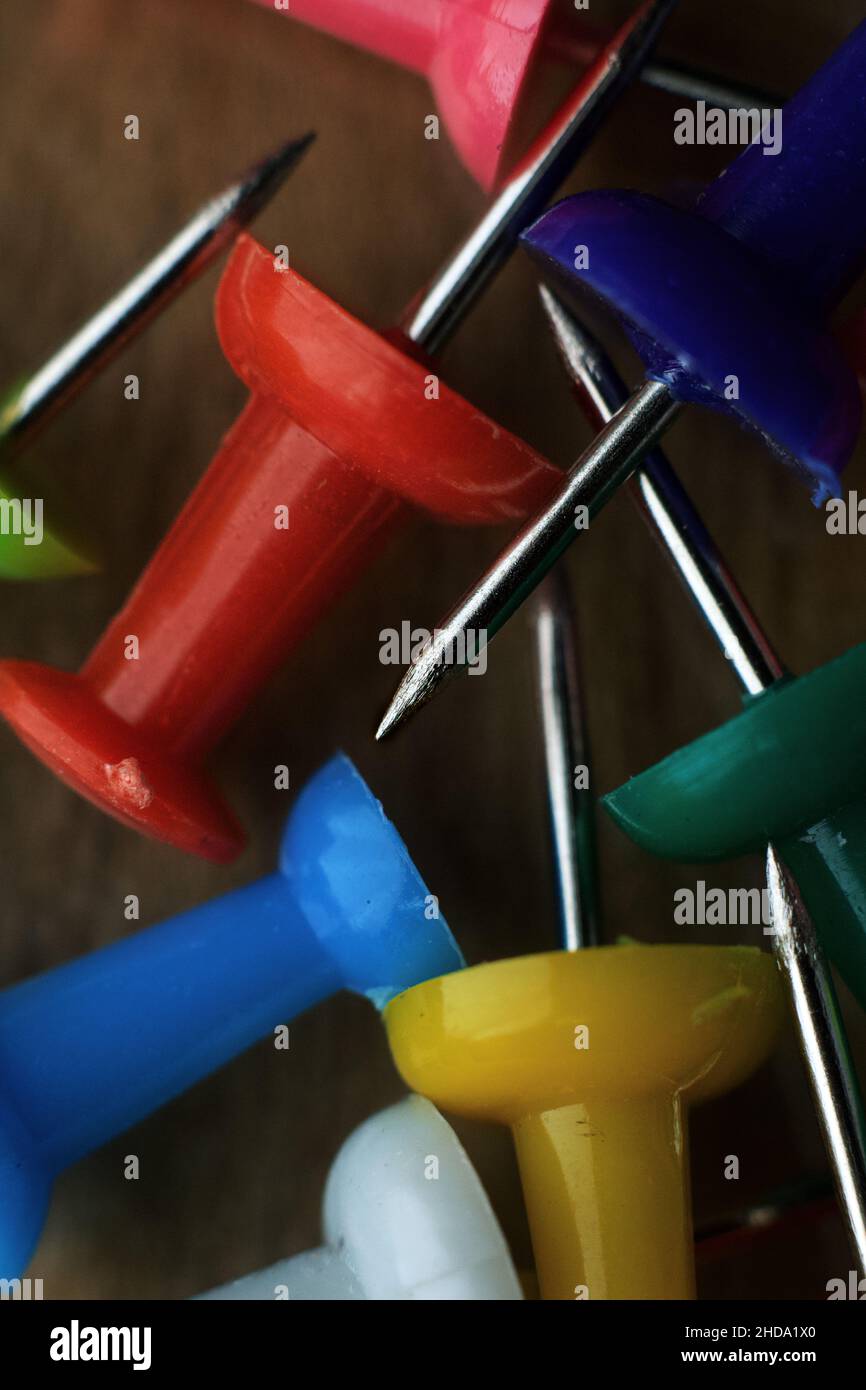 Vertical macro shot of multicolored pushpins on a blurry wooden background Stock Photo