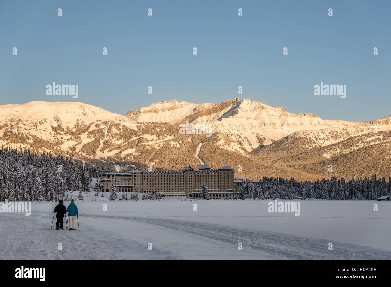 Lake Louise, AB, Canada-December 20, 2021: Couple cross country skiing on frozen lake with Chateau Lake Louise and snow covered mountains in backgroun Stock Photo