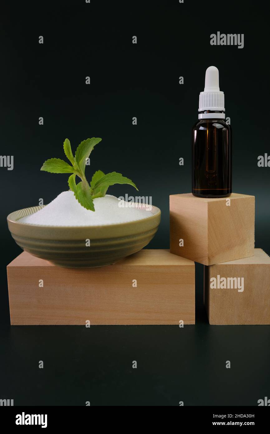 Dried stevia leaves, green branch and stevia liquid extract on wooden podiums on a green