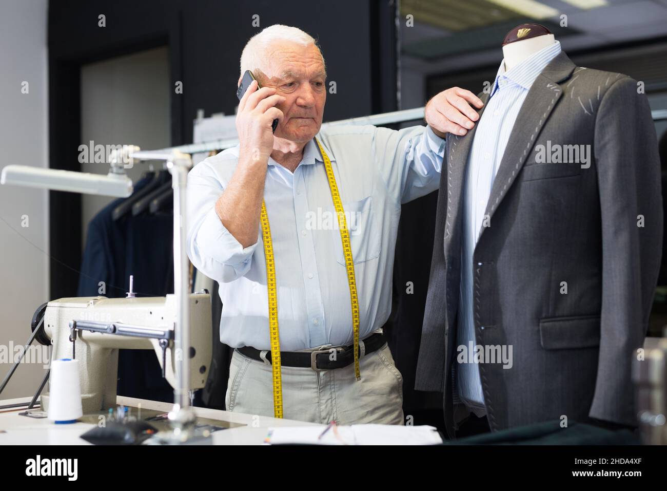 Professional tailor man talking on mobile phone and making notes in notebook Stock Photo