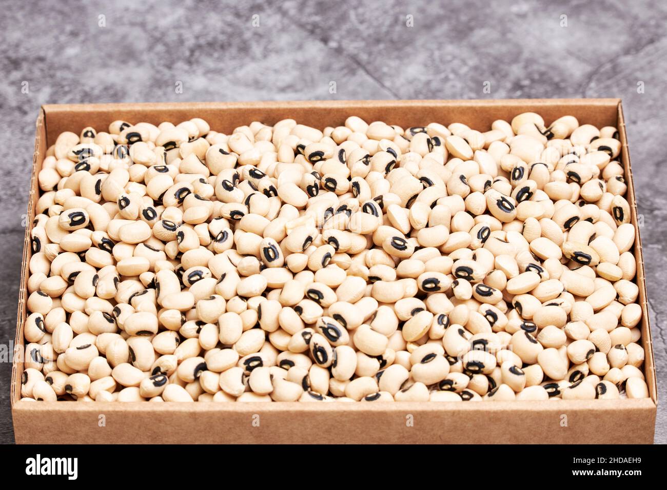 Pile of small raw white beans in a cardboard box on a gray stone background. Vegetarian health food Stock Photo
