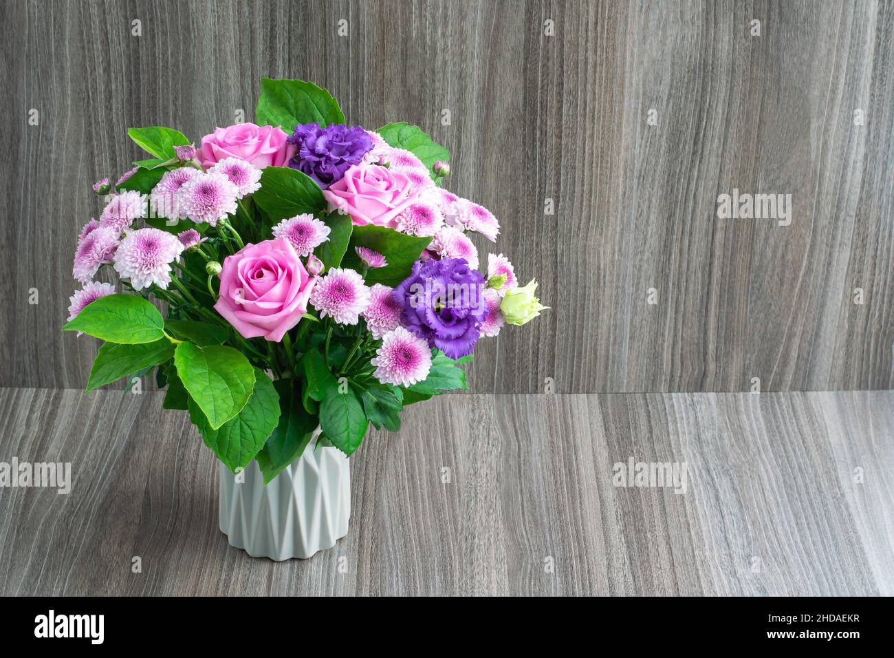 Flower arrangement in a small vase on a wooden background, copy space for text Stock Photo