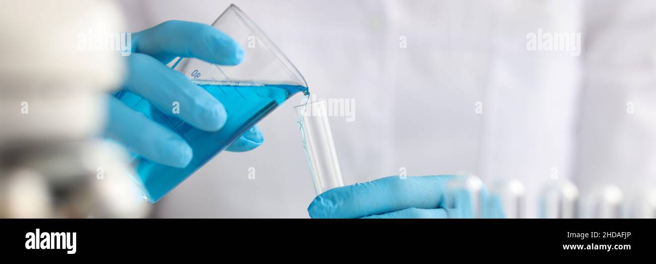 Scientist with gloves pours blue liquid into test tube in laboratory ...
