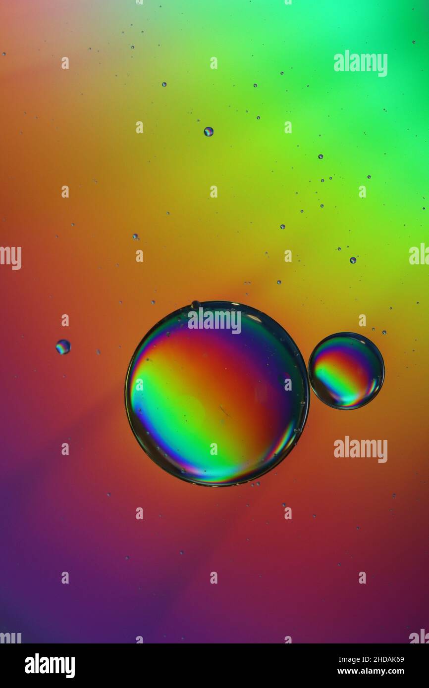 two oil droplets drift on a water surface and shimmer in beautiful ...