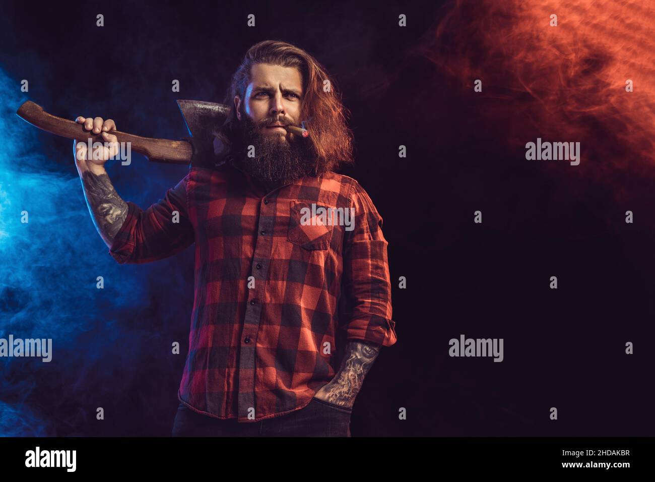 Handsome man holds old axe. Bearded lumberjack. Serious brutal man in checkered shirt with long hair Stock Photo