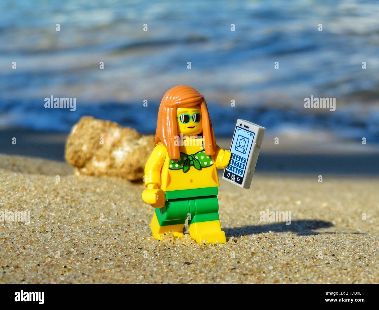 Closeup shot of a Lego toy walking on a beach wearing a bikini and holding  her phone Stock Photo - Alamy