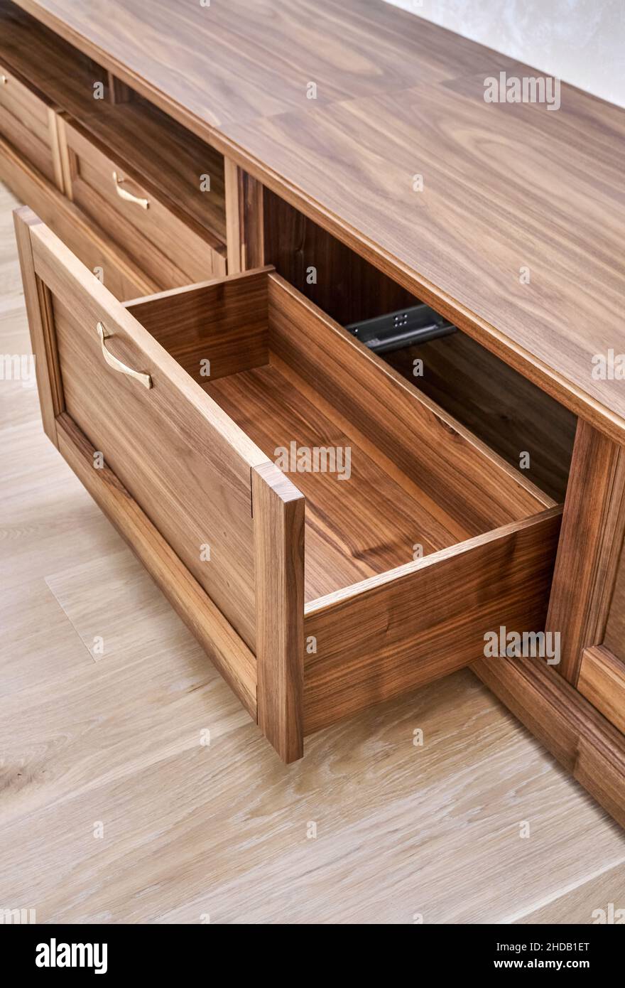 Elegant new TV cabinet made of veneer and solid walnut lumber with gold handles near wall in light room close upper view Stock Photo