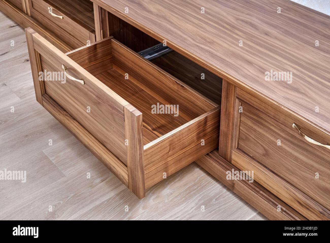 Elegant new TV cabinet made of veneer and solid walnut lumber with gold handles near wall in light room close upper view Stock Photo