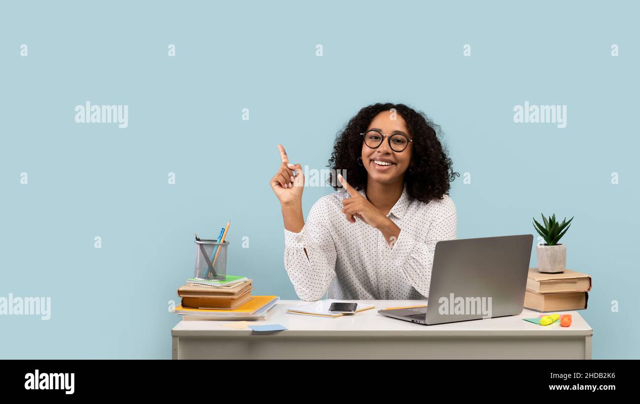 Happy young black female student sitting at desk with laptop and study ...