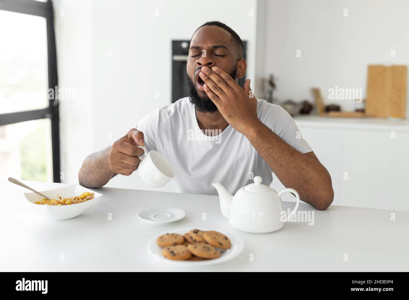 Black man yawning, pouring coffee away from cup Stock Photo