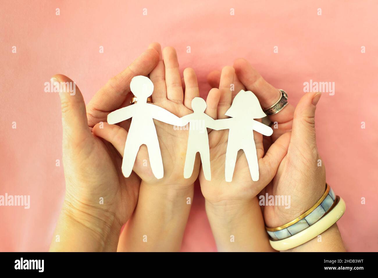 Cropped shot of mother, father and child holding family paper cut out in hands, isolated on pink background. cardboard figures of parents and kid hold Stock Photo