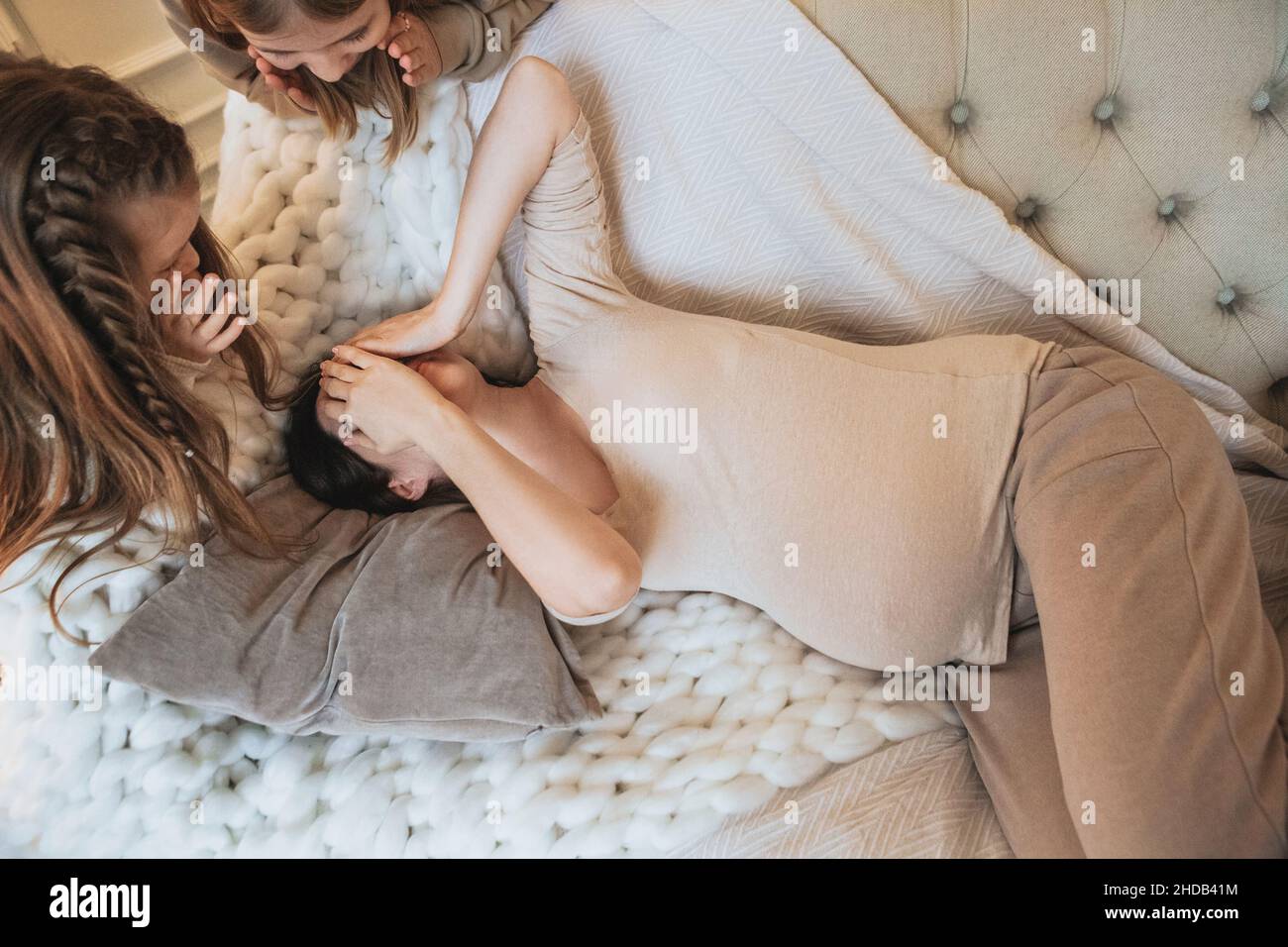 View from above of happy family pregnant woman and her two little daughters playing hide and seek at home, having fun during leisure time at home, mot Stock Photo