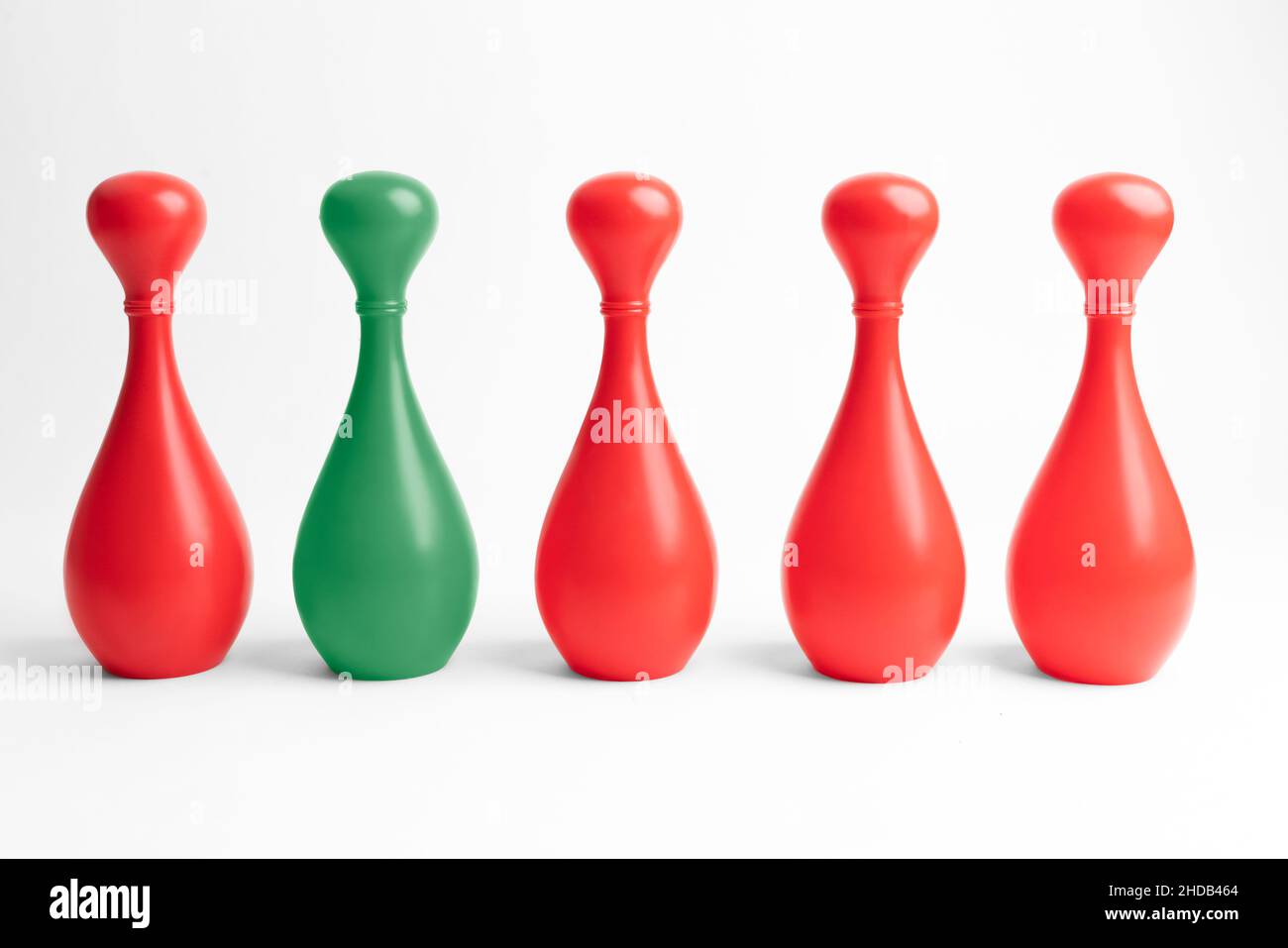 Four red and one green skittle in a row on white background. Teamwork with outstanding team member or leader. Dare to be different. Standing out from Stock Photo
