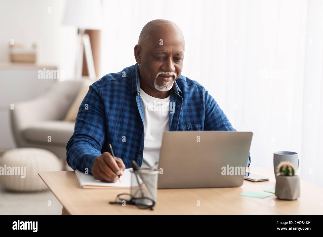 Senior Black Man Using Laptop Taking Notes Working At Home Stock Photo