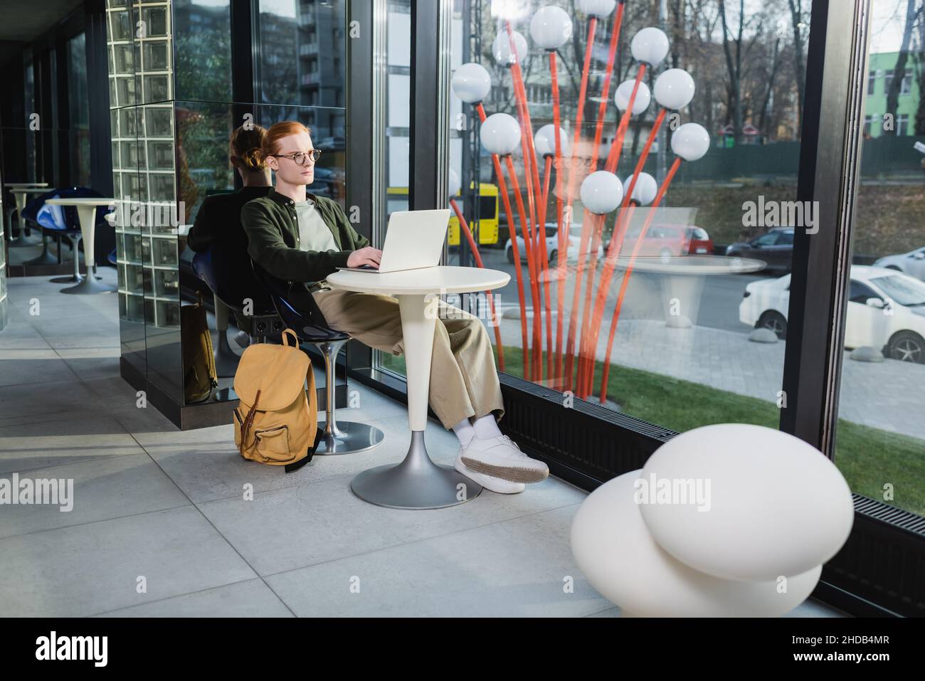 Redhead freelancer using laptop near backpack in hotel lobby Stock Photo
