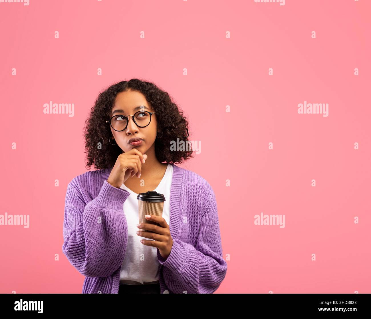 Pensive millennial African American female holding takeaway coffee and pondering on offer, looking aside at empty space Stock Photo