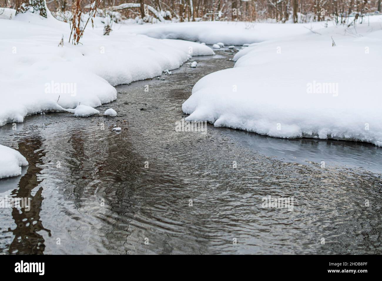 Winter landscape with an unstoppable stream of water (stream) surrounded by white snows. Stock Photo