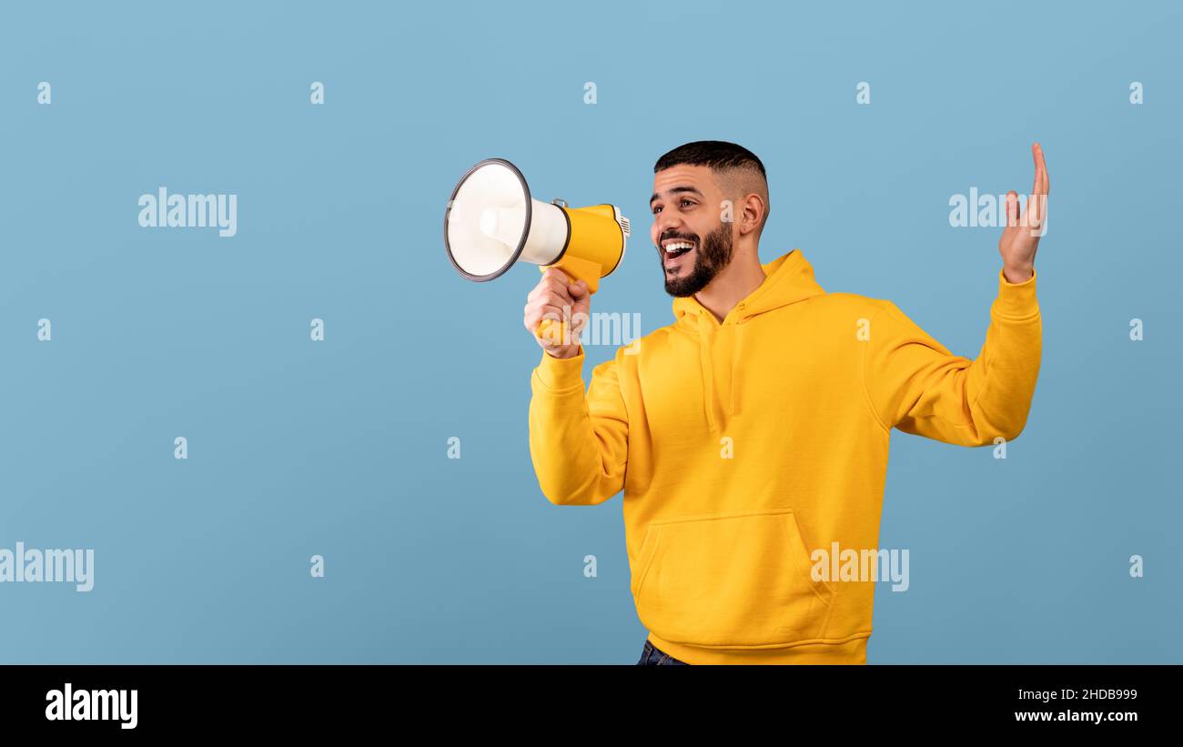 Promo announcement. Happy arab guy with megaphone in hands sharing news or interesting offer, blue background Stock Photo