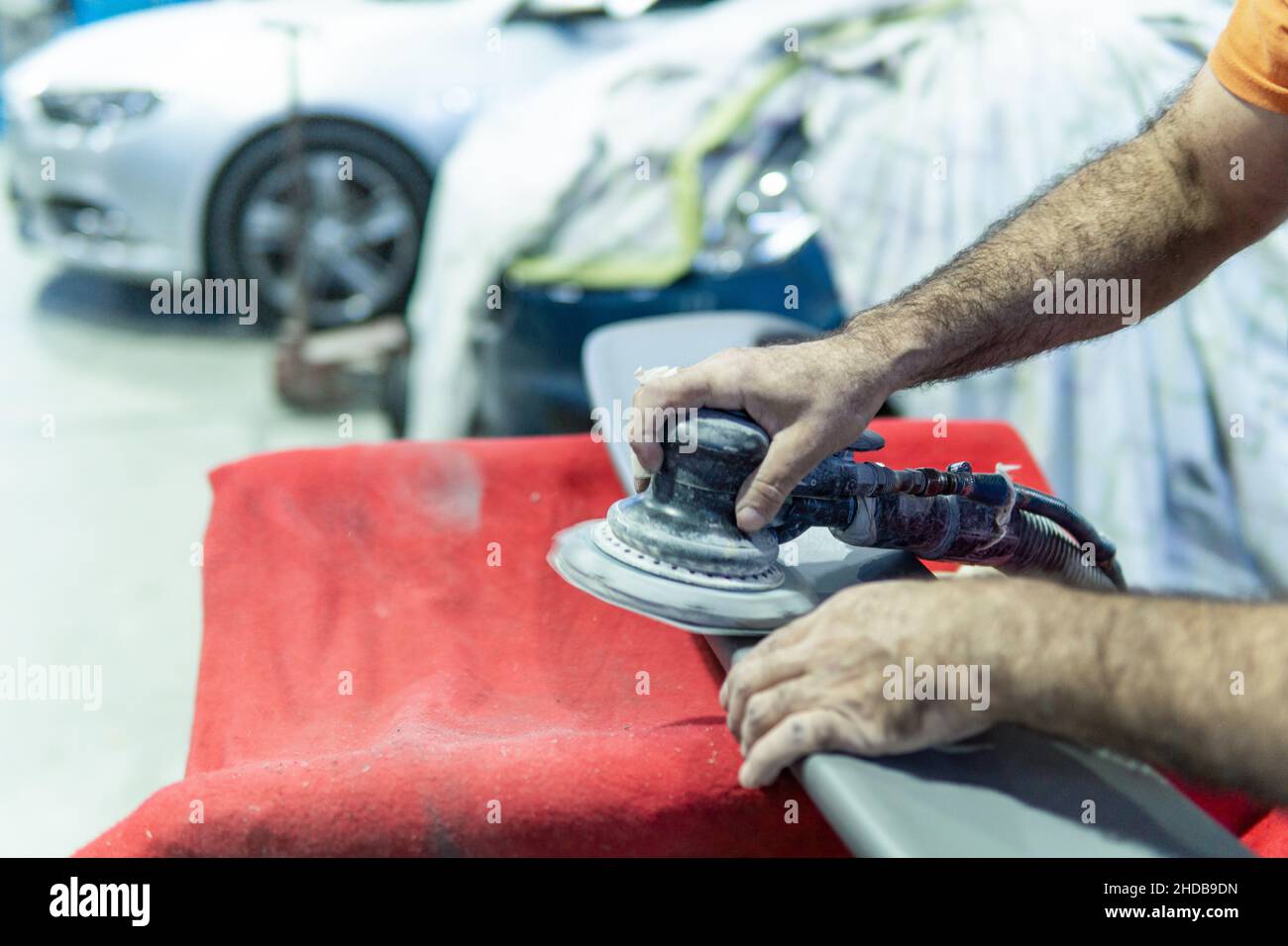 Auto mechanic sanding a part of a car in a garage. Preparing for painting the car in a workshop. Blurry movement Stock Photo