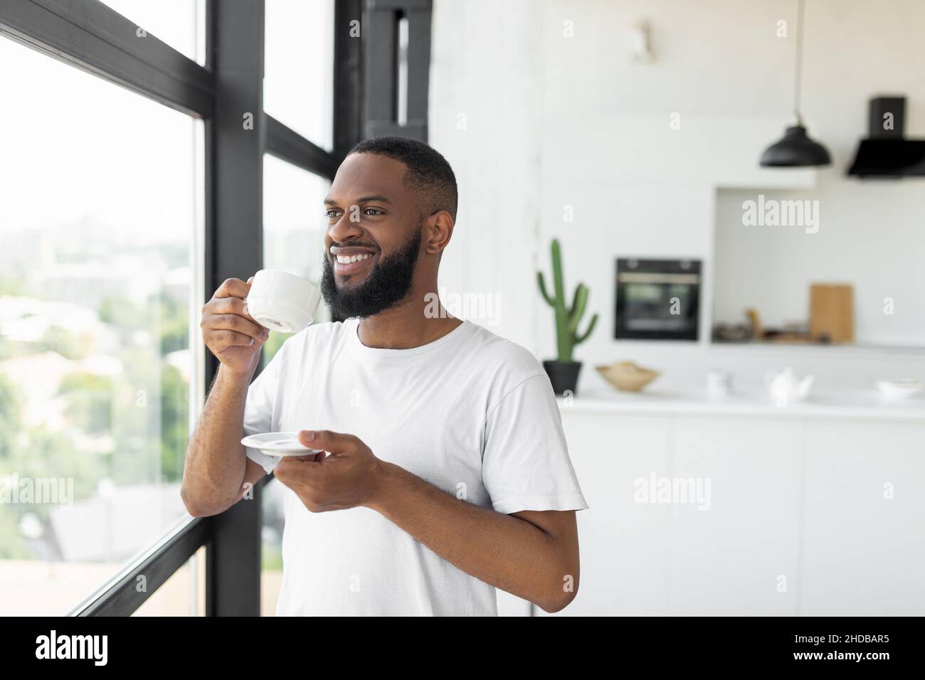 Smiling African American man drinking coffee looking through window Stock Photo