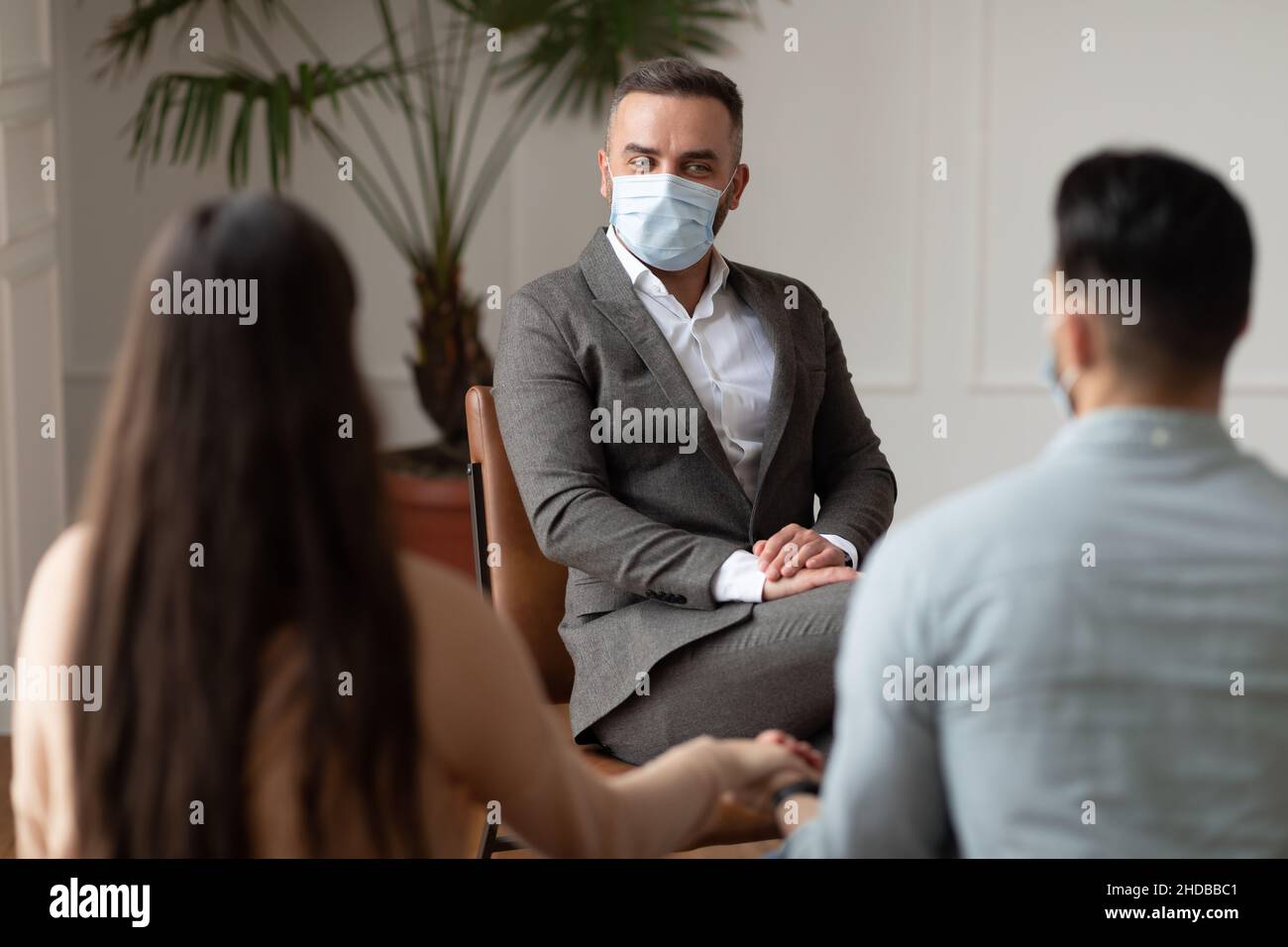 Young couple sitting at therapy session with therapist in facemask Stock Photo