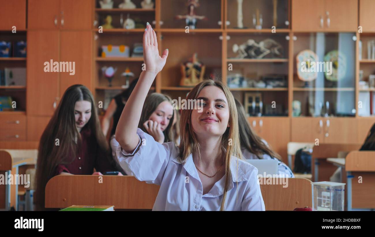 A girl student sitting at a desk raises her hand in the class Stock ...