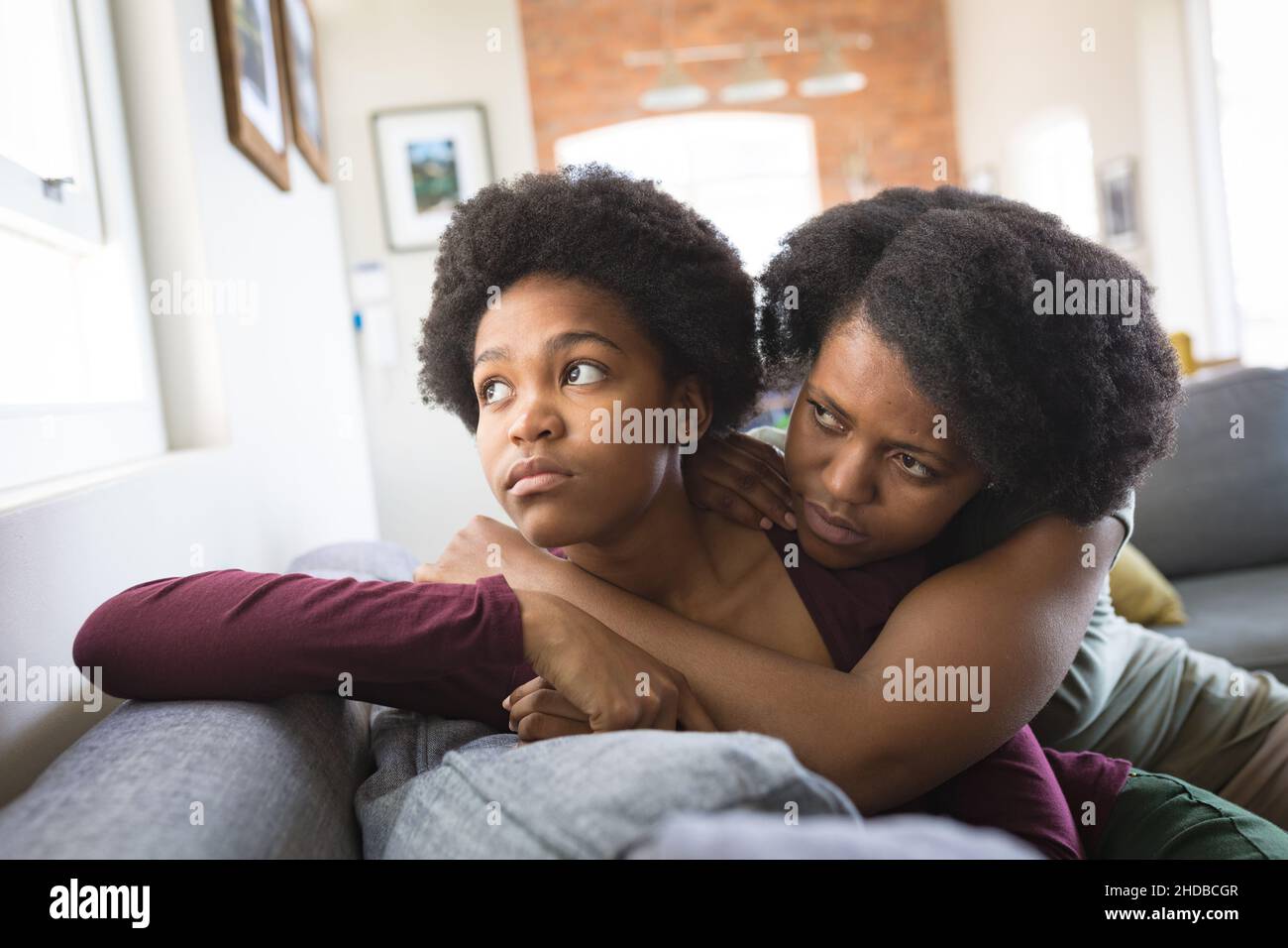 Thoughtful sad woman and daughter looking through window while leaning on sofa at home Stock Photo