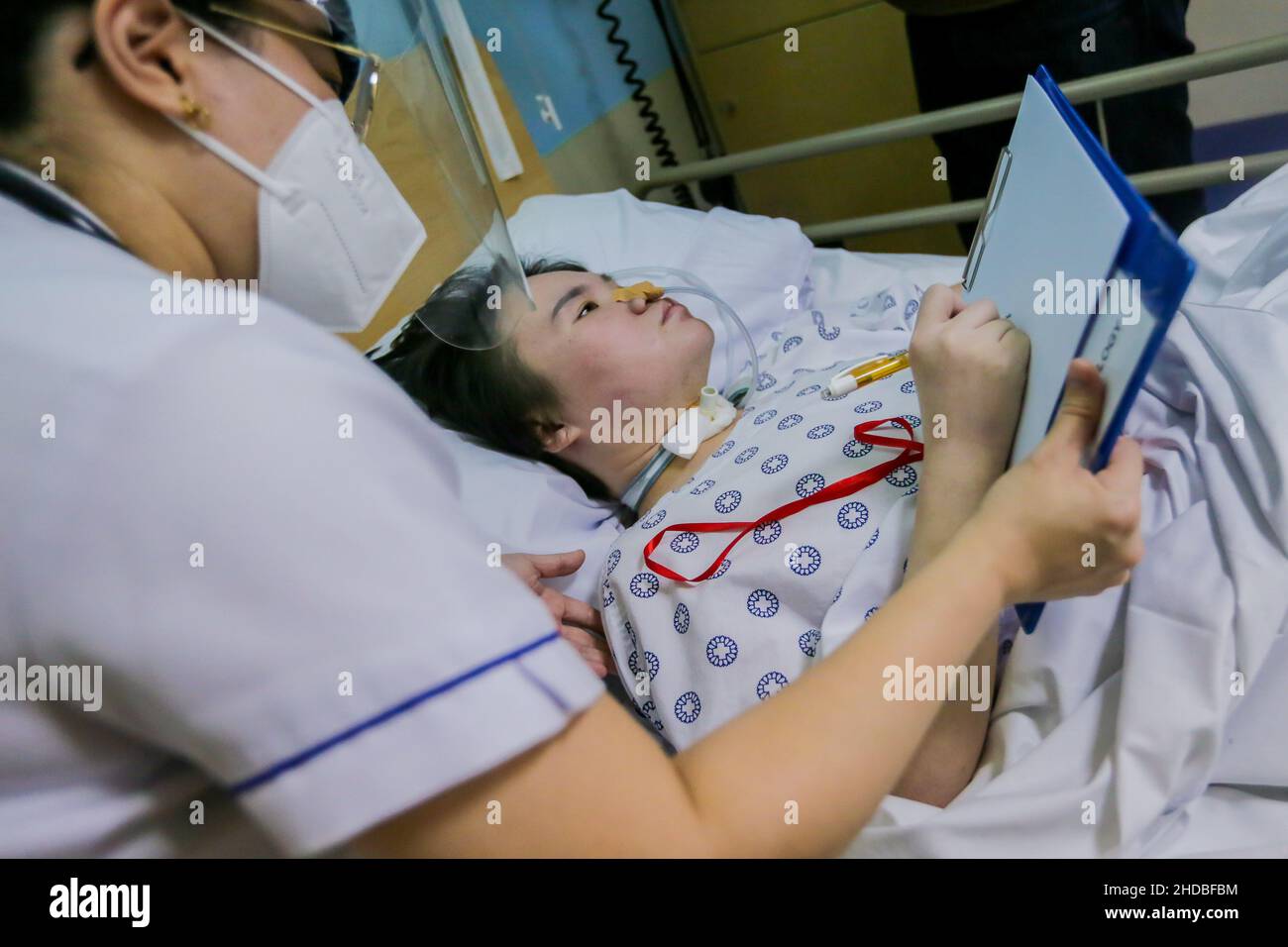 (220105) -- PASIG CITY, Jan. 5, 2022 (Xinhua) -- Li Jinxin, a 26-year-old Chinese woman, writes her name assisted by her nurse Sherricka Mae Navalta at the Medical City hospital in Pasig City, the Philippines, Dec. 13, 2021. Li Jinxin has found her dream of returning home come true after battling a devastating illness for almost two and a half years in the Philippines that nearly cost her life.   Li spent 904 days bedridden in Medical City due to a brain hemorrhage.    TO GO WITH 'Feature: With help of Filipino medics, once critically-ill Chinese woman gets back home' (Xinhua/Rouelle Umali) Stock Photo