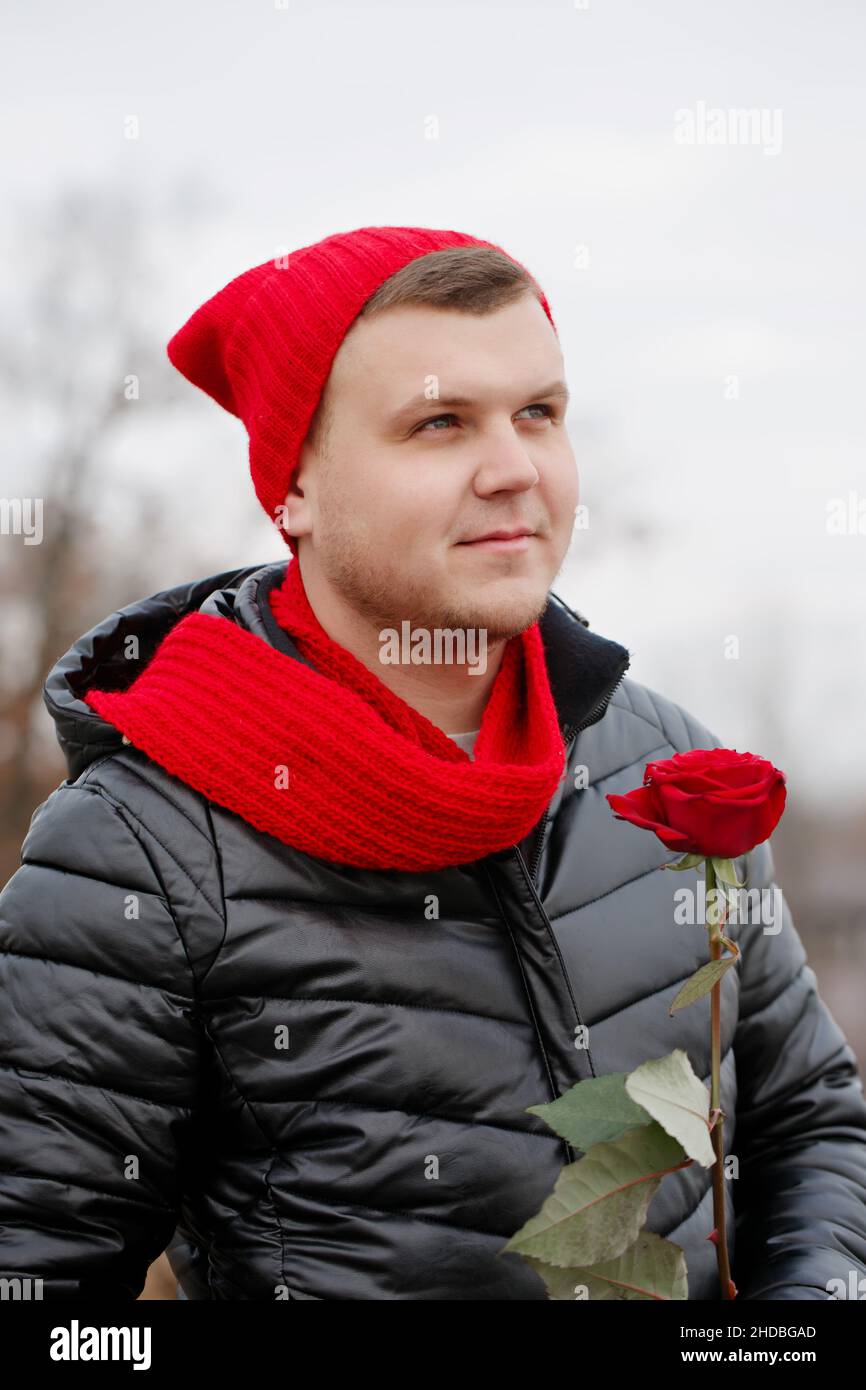 Handsome young man with red rose in hands outdoors in snowy weather. The concept for St
