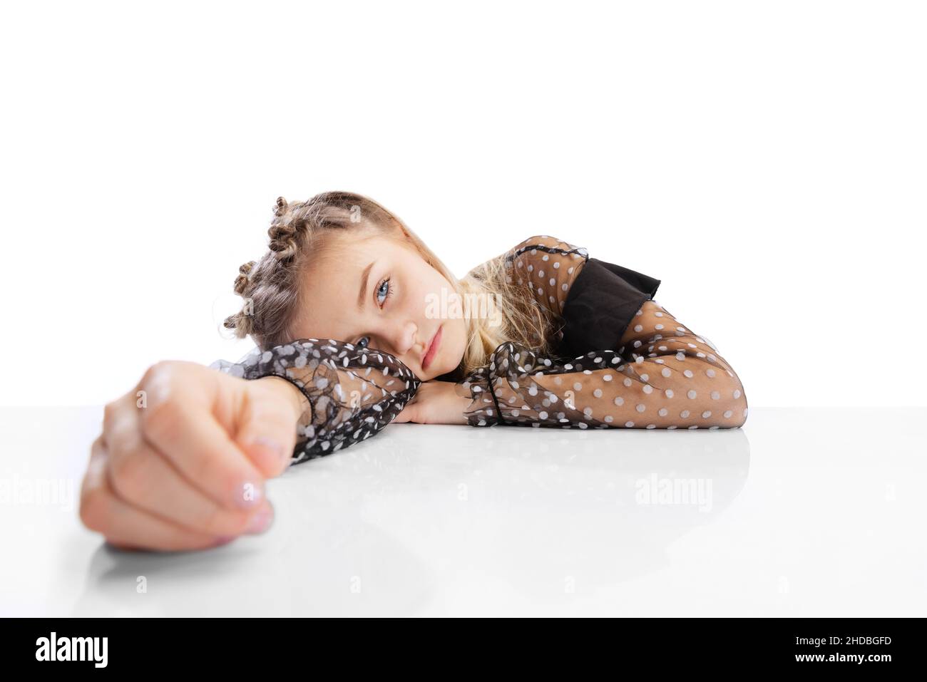 Close-up beautiful little cute girl, pupil in black dress sitting at table isolated on white studio background. Education, childhood concept. Stock Photo