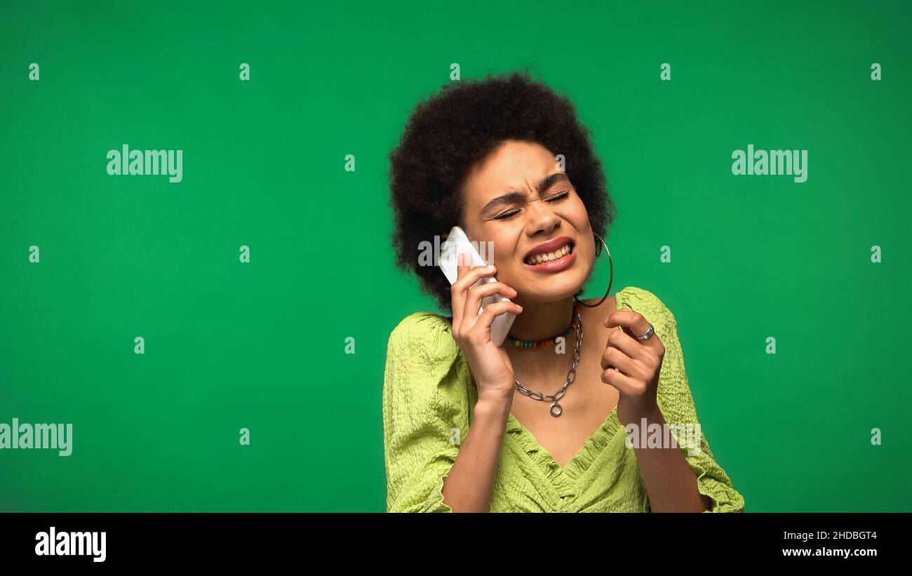 stressed african american woman in blouse talking on cellphone isolated on green Stock Photo