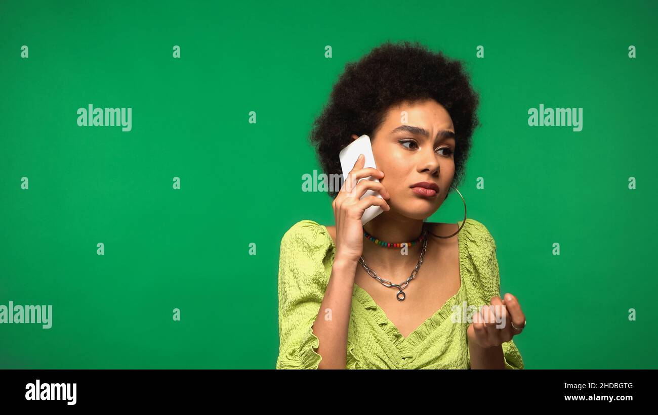 upset african american woman in blouse talking on cellphone isolated on green Stock Photo