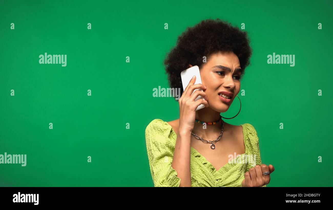 disappointed african american woman in blouse talking on cellphone isolated on green Stock Photo