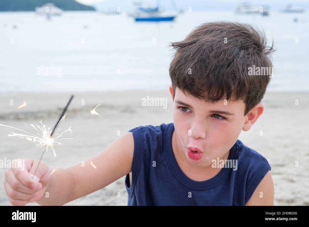 8 years old child looking and holding a candle sparkles in the sand on the beach. Stock Photo