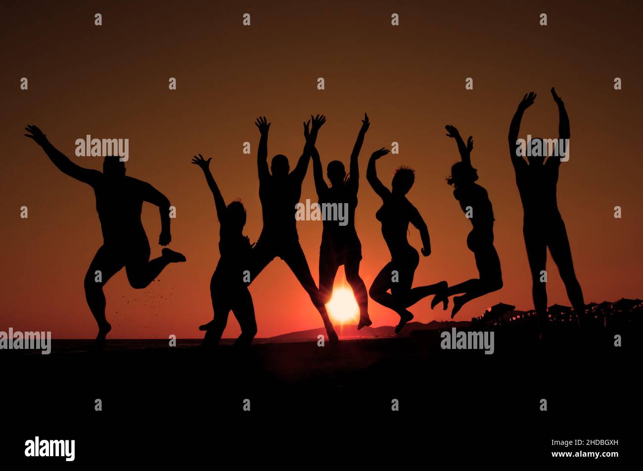 group of happy young people silhouettes jumping on the beach on ...