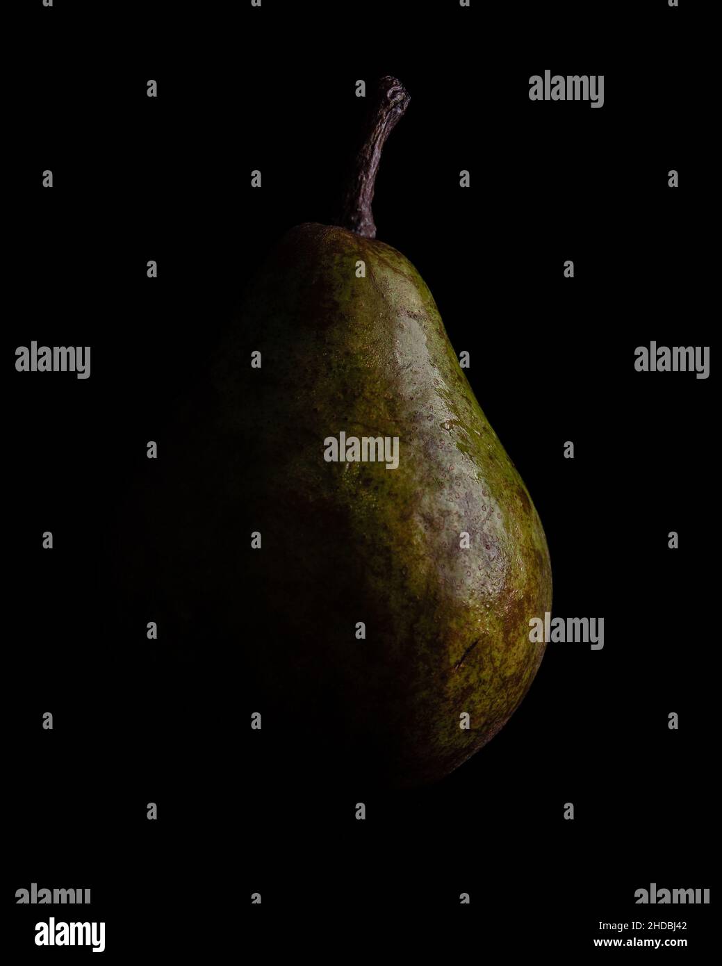 Vertical of a green pear darkened from the left side isolated on a black background Stock Photo