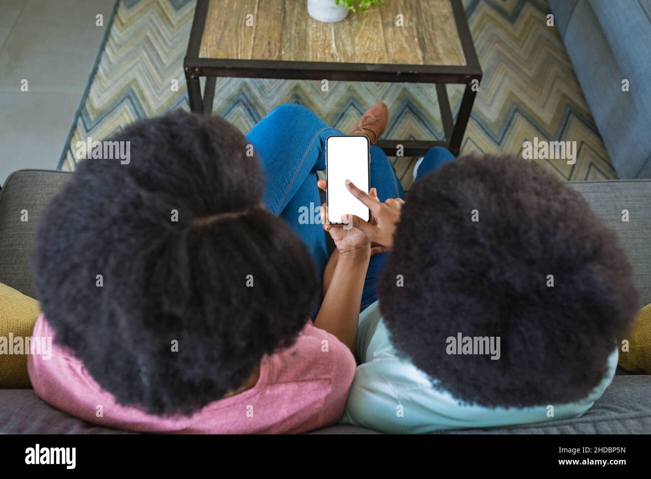 Teenage girl pointing at blank screen while teaching mother to use smart phone at home, copy space Stock Photo