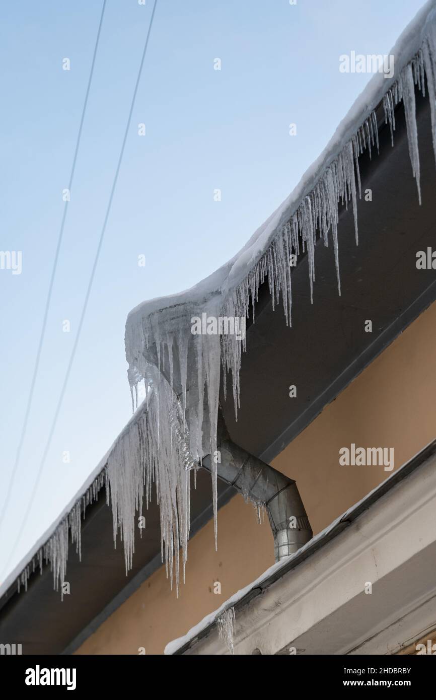 Big frozen icicles dangerously hanging from building edge on cold winter day. Ice dam on roof Stock Photo