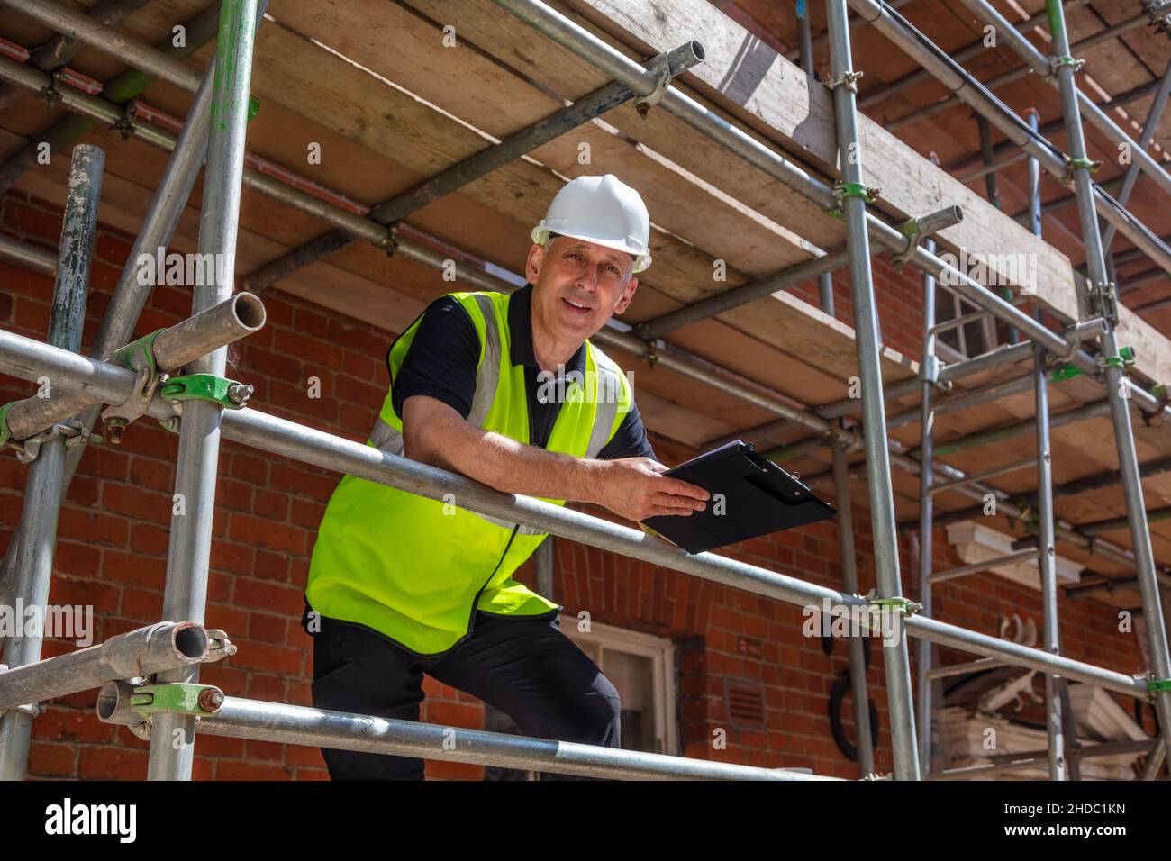 Male builder foreman, construction worker, contractor or architect on building site writing on black clipboard Stock Photo
