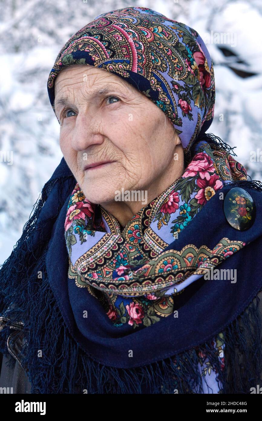 Portrait of a Russian elderly woman with a beautiful colorful Pavlo Posad head-scarf on blurred winter background. Stock Photo