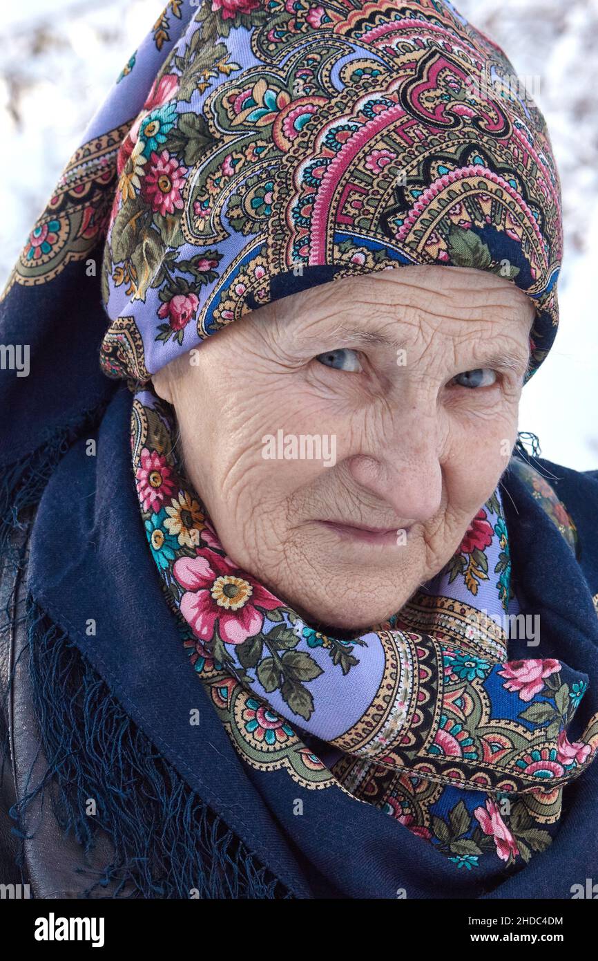 Portrait of a Russian elderly woman with a beautiful colorful Pavlo Posad head-scarf on blurred winter background. Stock Photo